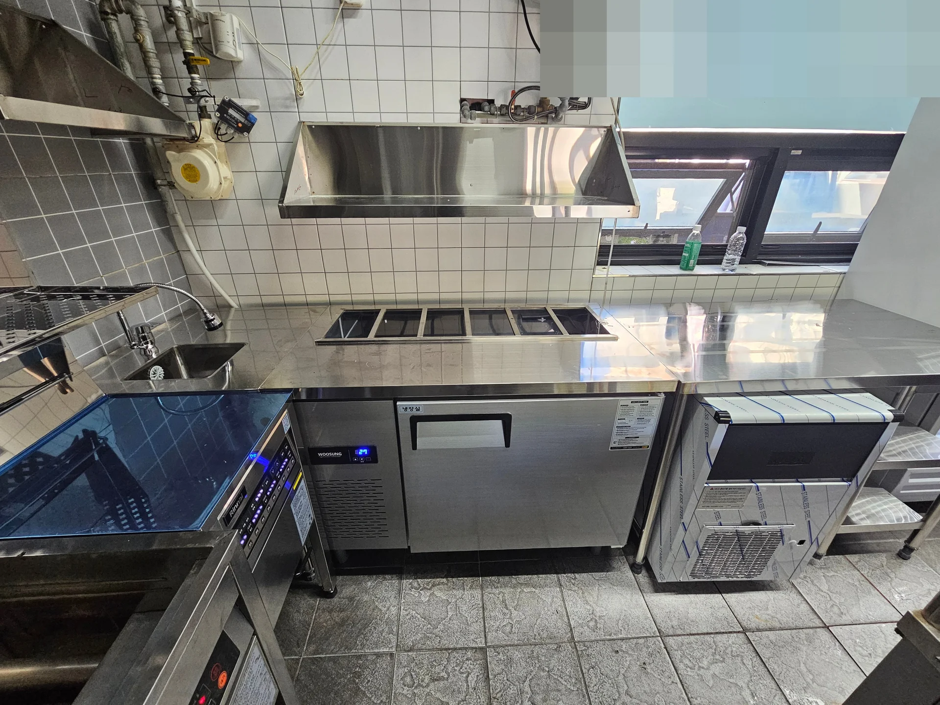후드 아래 냉장고와 제빙기가 이어진 우동집 주방 (창문 로고는 가림 처리)